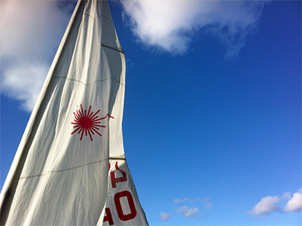 Laser sailboat sail blowing in the wind showing logo with blue sky background